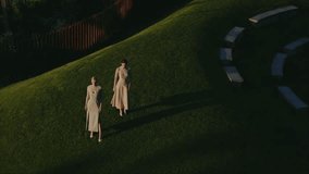 Two elegant women in long dresses standing on a grassy hill under the evening sunlight. The ambient setting evokes tranquility and serenity among the natural surroundings. - Powered by Shutterstock - Get 15% off with code: PIKWIZARD15