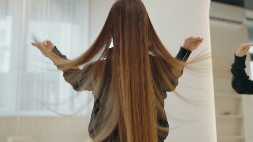 A woman with long, luxurious brown hair runs her fingers through it. She is facing away from the camera, highlighting the length and health of her hair. Modern Beauty Salon