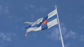 The state flag of Finland, featuring the blue Nordic cross and the Finnish coat of arms, is seen waving in the wind against a clear blue summer sky. - Powered by Shutterstock - Get 15% off with code: PIKWIZARD15