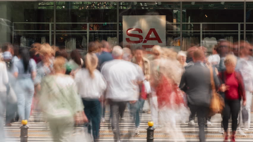 Time-lapse busy street near shopping mall entrance unrecognizable people crowd walking crosswalk. Rush hour crowded shopping center, shop window, fast motion, blurred faces