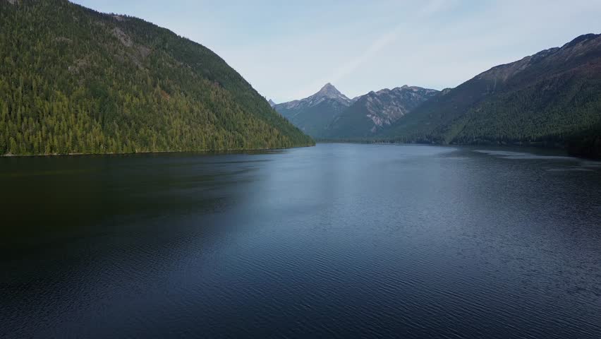 Misty Chilliwack Lake in British Columbia, Canada, with calm waters reflecting pine forests and distant mountain peaks under cloudy skies.Photo taken on 20-03-2025