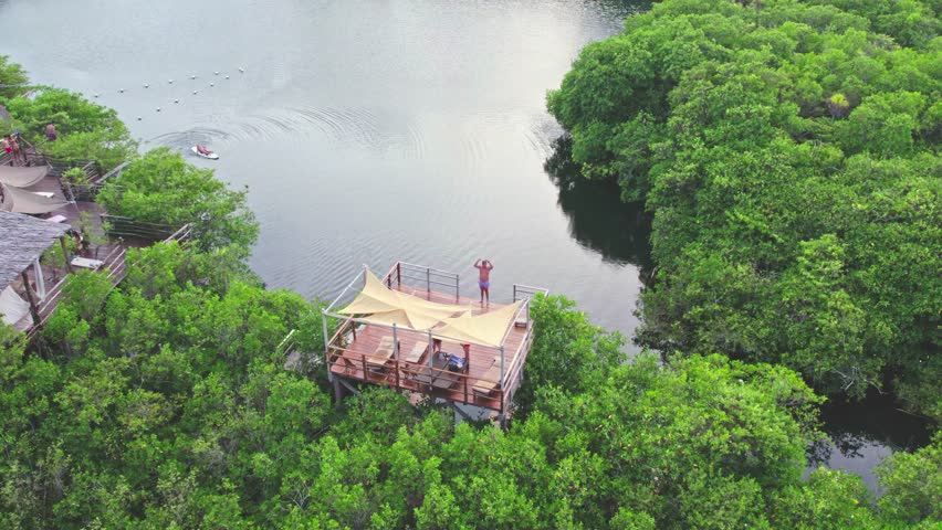 Scenic Aerial Drone View of a person jumping  off a wooden platform in a Cenote in the  Jungle, Tulum Mexico, having fun during summer holidays