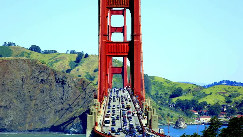 Golden Gate Bridge spans across water, connecting San Francisco to Marin County. Vehicles traverse this iconic transportation route under clear blue sky.