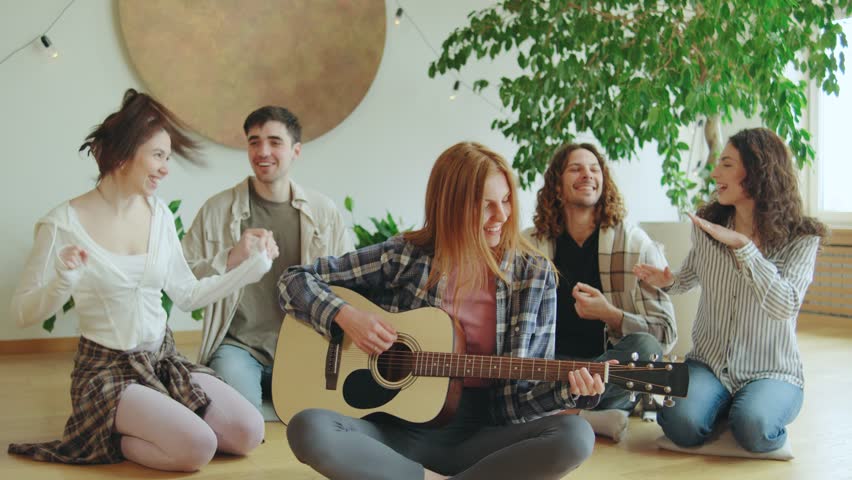 Group of friends enjoying acoustic music together in a cozy indoor setting during a relaxed afternoon gathering