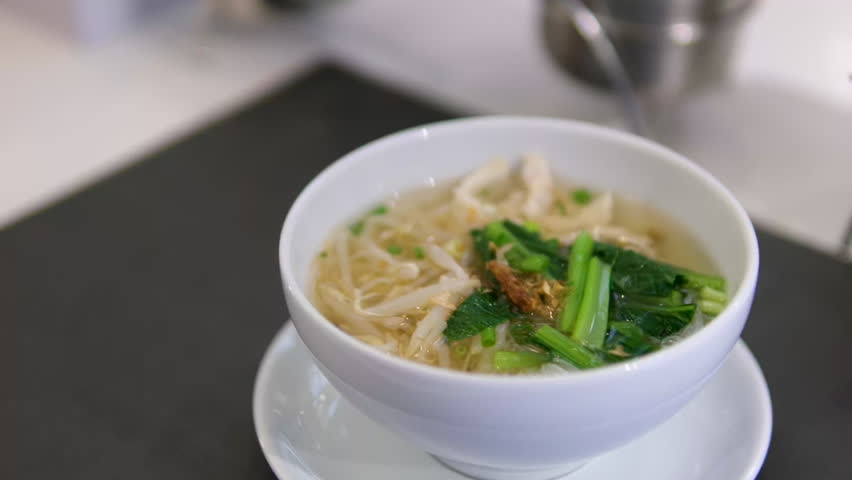 A steaming bowl of Pho, a traditional Vietnamese noodle soup, garnished with fresh herbs, chili peppers, and beef meatballs. The appetizing broth and vibrant ingredients create a delicious visual.
