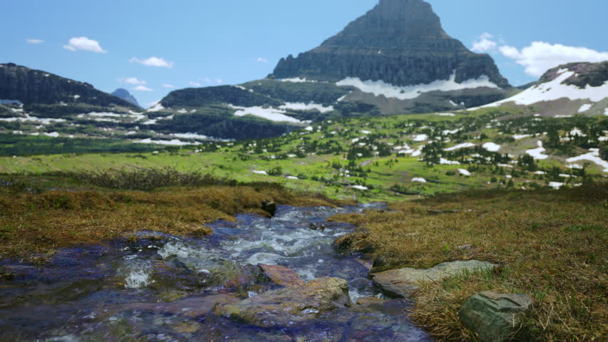 Glacier National Park in Montana features stunning landscapes of majestic mountains, flowing streams, and vibrant greenery, capturing the essence of natures beauty and splendor in every season