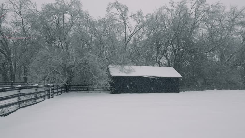 Pan shot of country barn building and fence during snowstorm in Kentucky