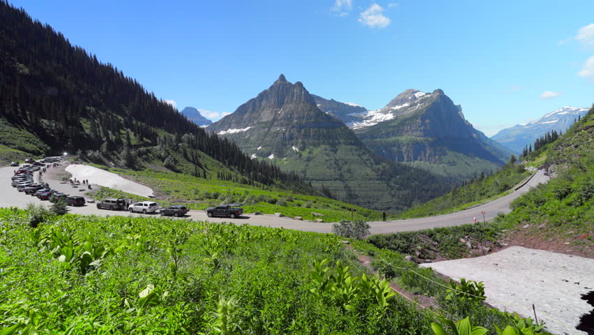 Experience the breathtaking panoramic views of Glacier National Park, featuring its rugged mountains, lush greenery, and the meandering winding roads that enhance the natural beauty of the area