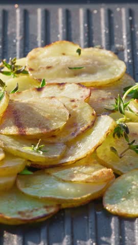 outdoor cooking. cook preparing sliced potatoes with oil on hot grill pan for making delicious meal in garden, food closeup, outdoors natural light