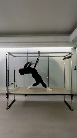 A focused woman performs challenging Cadillac Pilates exercises, enhancing strength and flexibility indoors. This video captures a dynamic fitness routine for improving health and wellness