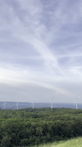 Aerial footage of Lam Takhong Dam in Nakhon Ratchasima, Thailand, featuring large wind turbines generating renewable energy. Scenic view of the reservoir, green hills, and clean blue sky.
