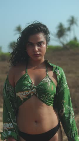 Woman in a tropical green top and black bikini standing on a sunny beach
