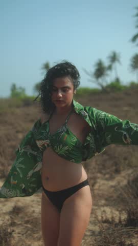 Young woman in tropical shirt dancing on the beach, carefree and joyful