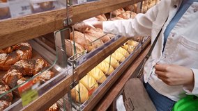 Customer selects freshly baked multigrain bread using gloves in a bakery. Variety of artisan loaves displayed behind glass in a self-service section of a modern grocery store. Daily fresh crusty bread - Powered by Shutterstock - Get 15% off with code: PIKWIZARD15
