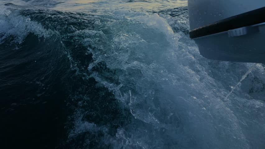 Summer night at sea. An outboard motor propels a boat forward; producing air bubbles wake.
