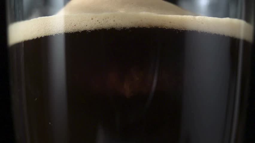 Rich dark coffee swirling in glass with white milk head and bubbles rising in slow motion against a black background
