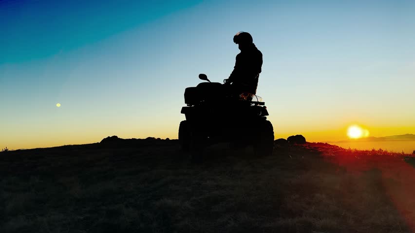 Silhouette of ATV Rider on altitude mountain peak during stunning sunset
