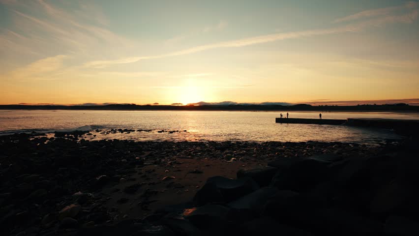 Golden sunset over sandy beach with people in silhouette stock footage