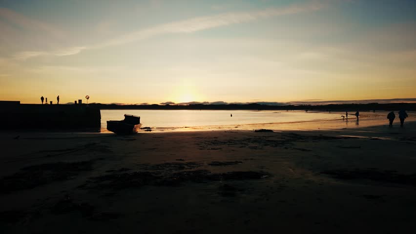 Golden sunset over sandy beach with people in silhouette stock footage