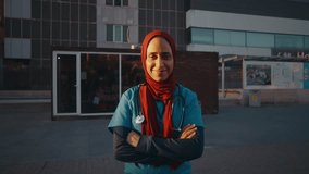 Professional muslim female doctor wearing hijab, confidently standing outside hospital, smiling with crossed arms while representing healthcare diversity and expertise - Powered by Shutterstock - Get 15% off with code: PIKWIZARD15