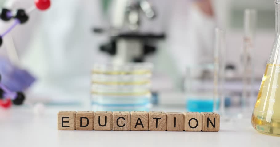Wooden cubes spell Education resting on lab table beside yellow fluid in flask. Out-of-focus background supports idea of science meeting learning