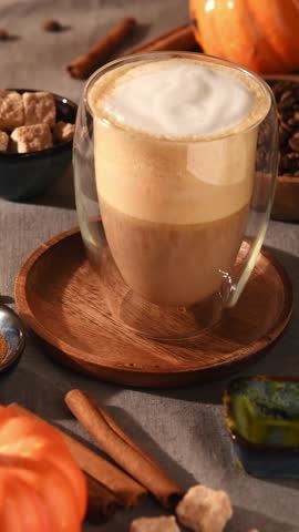 Pumpkin latte in glass mug topped with cinnamon on creamy foam, cozy autumn vibes with spices, sugar cubes and soft warm light.