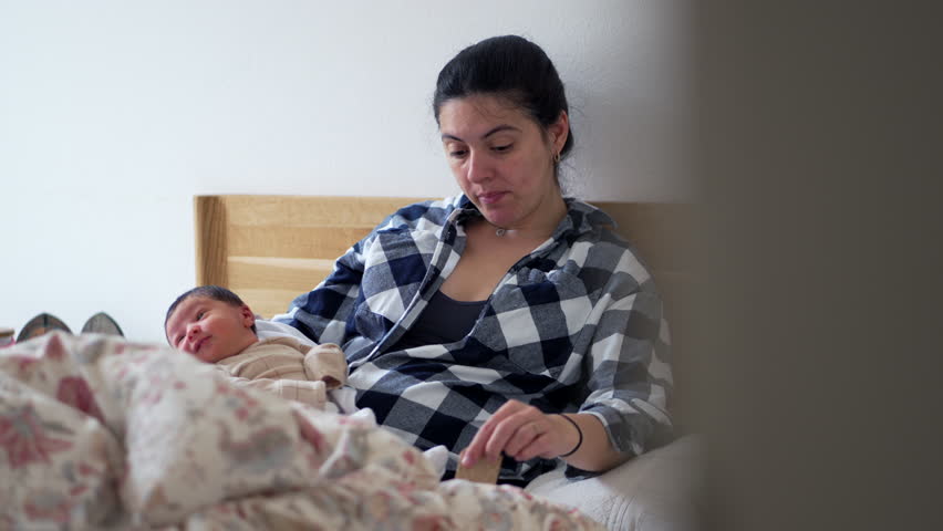 Mother with newborn baby resting on bed, looking tired and contemplative, highlighting the challenges and tender moments of early motherhood, candid snapshot of family life and care