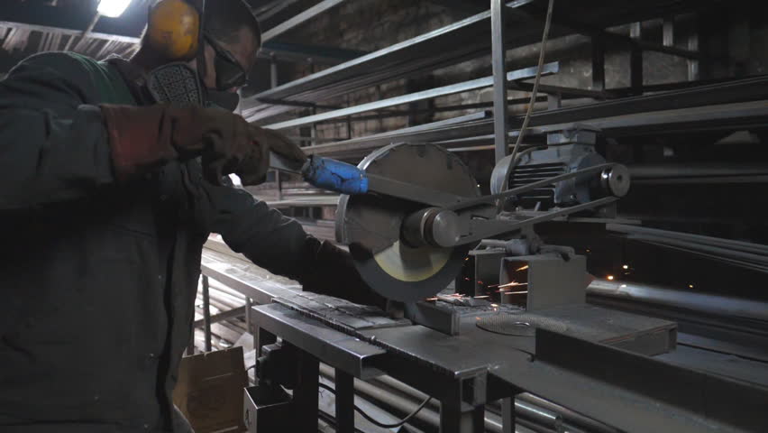 Industrial worker with circular saw sawing steel in workshop. Man in safety protection wear use saw cutting machine to cut metal. Craftsman grinding metal. Sparks fly from hot metal. Slow motion