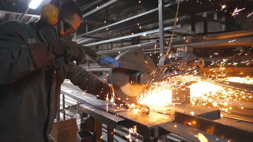 Industrial worker with circular saw sawing steel in workshop. Man in safety protection wear use saw cutting machine to cut metal. Craftsman grinding metal. Sparks fly from hot metal. Slow motion