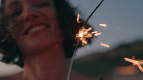 Closeup of young woman smiling and holding a sparkler at sunset. Sparkler burning brightly in the foreground. Happy, carefree, and joyful. - Powered by Shutterstock - Get 15% off with code: PIKWIZARD15