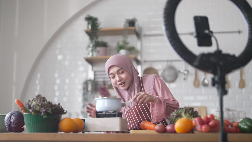 Muslim woman vlogger live streaming cooking online in kitchen look at camera with vegetables, content creator culinary class at home studio, halal food influencer cooking live, video for social media