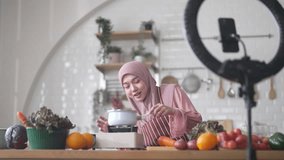 Muslim woman vlogger live streaming cooking online in kitchen look at camera with vegetables, content creator culinary class at home studio, halal food influencer cooking live, video for social media - Powered by Shutterstock - Get 15% off with code: PIKWIZARD15