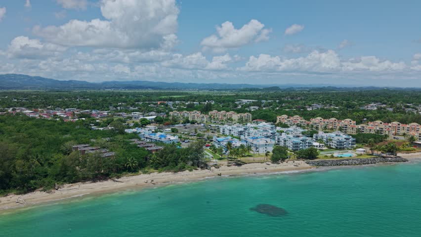Pan drone shot of Loiza cityscape with sand beach, Atlantic Ocean and blue sky during the day in Puerto Rico, USA