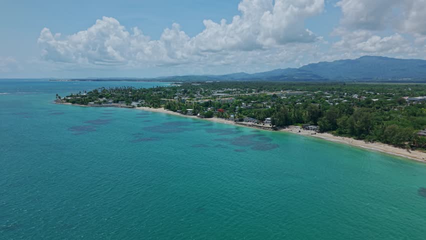 Establishing drone shot of Loiza cityscape with sand beach, Atlantic Ocean and blue sky during the day in Puerto Rico, USA