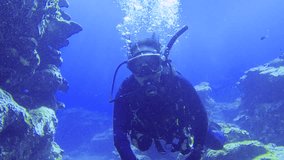 selfie camera view of a scuba diver wearing diving gear swimming through a under water narrow small cave gap between coral reef rocks toward other divers in front in blue ocean sea bottom during day  - Powered by Shutterstock - Get 15% off with code: PIKWIZARD15