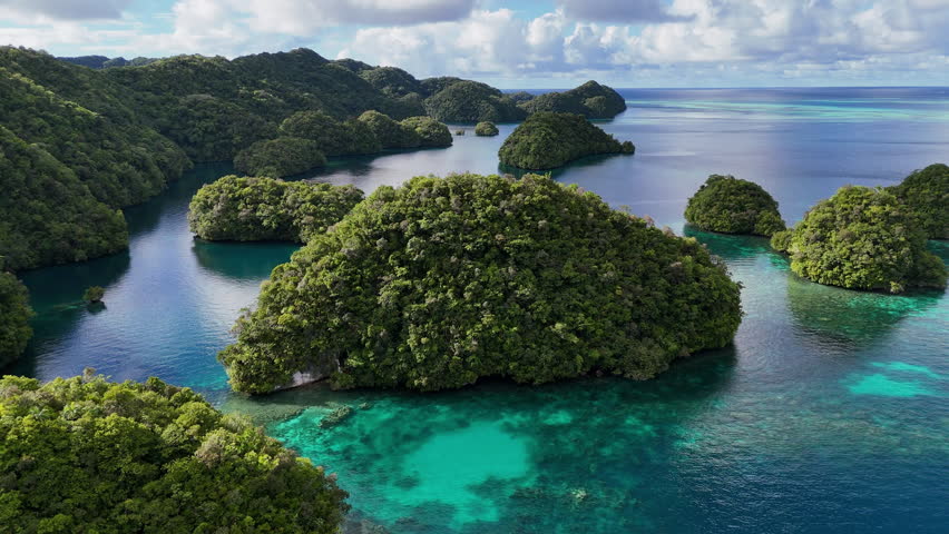 Scenic drone shot circling and revealing the pristine turquoise sea and lush islets of Palau. Orbiting drone shot of a large island of Palau.