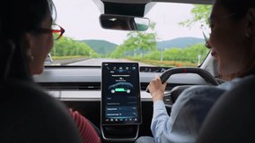 Happy beautiful asian woman friends driver electric car along a scenic winding road, surrounded by lush greenery. The digital touchscreen displays the car's battery level and charging options. - Powered by Shutterstock - Get 15% off with code: PIKWIZARD15