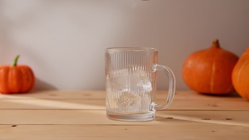 Golden pumpkin syrup is poured over ice in a clear glass mug, creating the cozy autumn mood for a homemade seasonal latte.