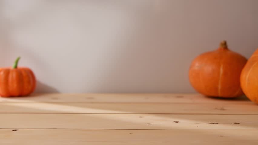 Hand places glass mug with iced pumpkin latte on sunlit wooden table with pumpkins, bringing cozy autumn mood and inviting to enjoy.