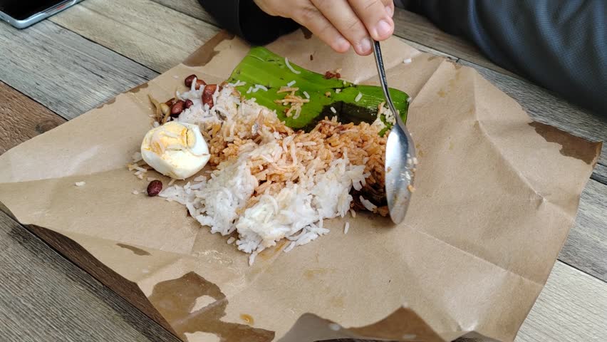 A woman enjoys nasi lemak bungkus, Malaysia's popular, quick breakfast. This simple meal, with egg and sambal, comes conveniently wrapped in paper for easy portability.