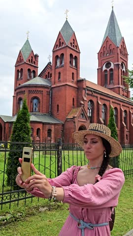 woman in pink dress and hat taking photo of herself against medieval building, girl taking selfie against building, travel around europe
