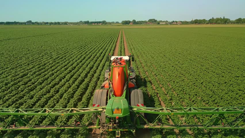 A Drone footage of a tractor spraying the crop with crop protection products in a sunny field