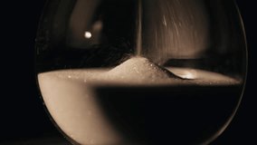 Closeup sand falling in hourglass standing dark room. Gold grains flowing inside transparent glass clock measuring time indoors. Elegant timepiece capturing minutes hours. Aesthetic timekeeper concept - Powered by Shutterstock - Get 15% off with code: PIKWIZARD15