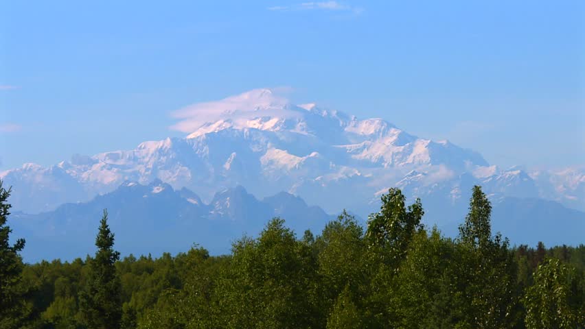 Mount Denali with lush forested foothills and distant glaciers in Denali National Park, Alaska. Static shot in daylight.