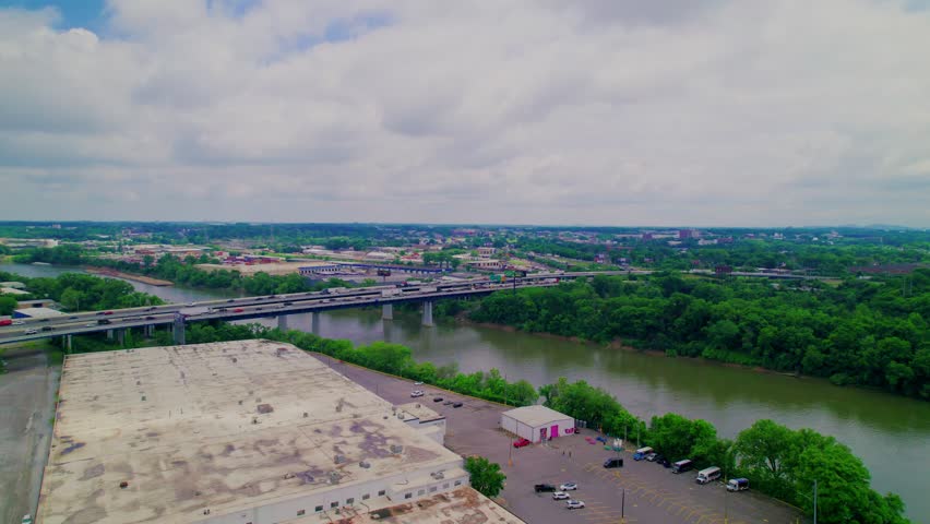 Wide drone view of Nashville, TN showcasing an interstate bridge crossing the Cumberland River, dense greenery, and surrounding development.