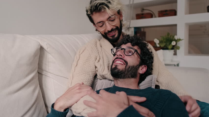 Two men, a gay couple, relax on the couch at home, enjoying each other's company. They look happy and in love.