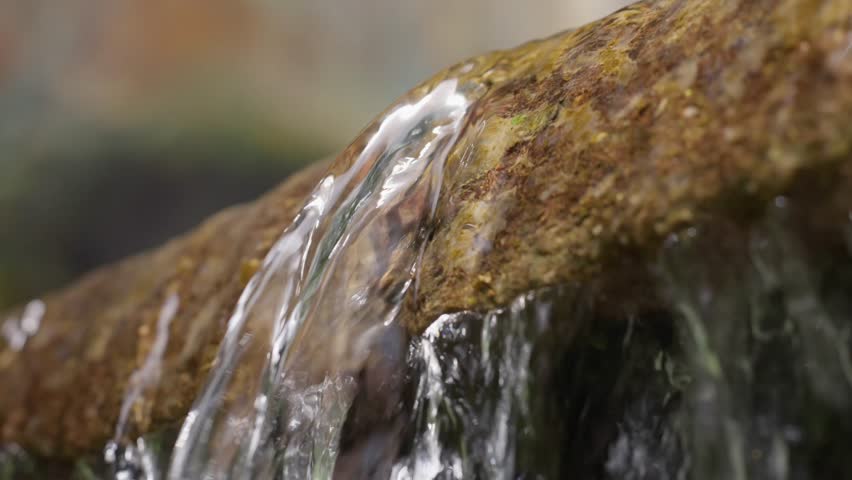 Detailed close-up showing clear water gently flowing over a textured stone surface outdoors.