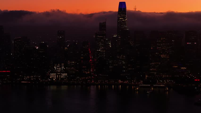 Aerial view of the San Francisco skyline at dusk, a symphony of lights and shadows, with the Salesforce Tower piercing through the clouds, San Francisco, California, United States.