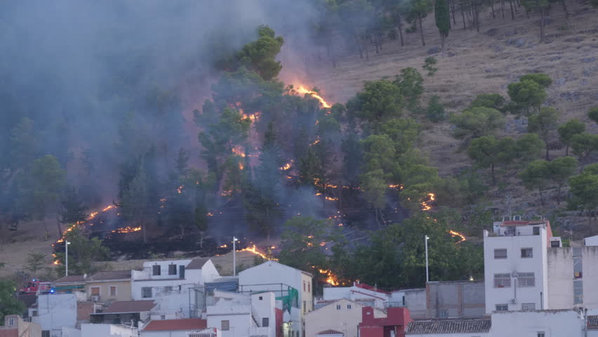 Forest fire in the pine forests of Jaén, Andalusia, Spain. The fire devours vegetation, with thick smoke hanging over houses.