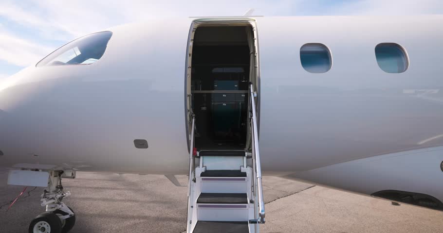Open cabin entry door and stairway of private jet on tarmac, showcasing luxury.